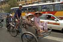 Passengers riding in a cyclo in heavy traffic down a busy street