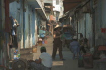 View down a side street with a woman wearing a conical hat and people sat on the ground