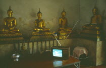 Thai boxing on television inside a monastery in front of seated Buddha figures.