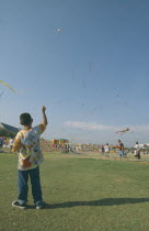 Kite festival at Sanam Luang  February. Boy flying one in foreground  many others in sky.