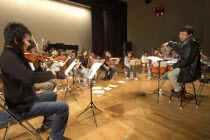 Conductor and music teacher talking to teenage first violin player in rehearsal of United Freedom Orchestra for spring concertmusic teacher Satoshi Miyano  MR13  talks to first violin Koji Katsuyama...