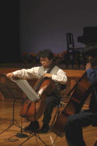 Music teacher playing the cello on stage as part of his students spring concert in the United Freedom OrchestraMusic teacher Satoshi Miyano  MR 14