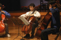 Music teacher playing Cello on stage with two of his students at spring concertSatoshi Miyano  music teacher  MR 13