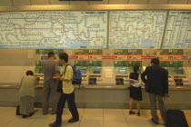 Tokyo station commuters at a row of ticket machines with route map above