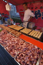 Narita Gion Festival. A man in a booth selling Tako Yaki and octopus dumplings with the ingredients including octopus in a line at the front and cooking dumplings at the rear.
