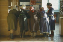 Group of women leaning on wooden shop counter to talk.