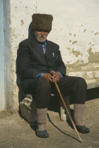 Elderly local man sitting outside wall of building.