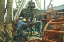 Workers using drill on oil rig.