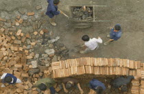 Construction site.  Looking down on workers stacking bricks and moving rubble.