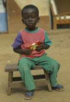 Portrait of young child sitting on wooden stool holding packet of chocolate.
