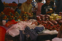 Sleeping child on market stall selling fruit.