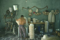 Panama hat industry.  Male worker operating machinery with hats stacked on floor and table beside him.