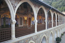 Tourist visitors in courtyard of monastery with religious mosaics decorating length of wall of first floor arcade seen on left.