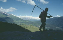 Silhouetted figure of man carrying scythe with mountain backdrop.