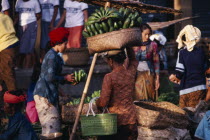Early morning market.  Woman carrying large basket of green bananas on her head.