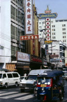 Street scene with tuk tuk and other traffic high rise buildings and advertising hoardings.