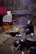 Kazakh woman inside her Kigizuy or yurt with covered stove and kettle suspended over small open wood fire.tent domestic interior  home Ger