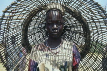 Portrait of young Dinka woman with fishing basket behind her casting shadow pattern over her face and upper body.