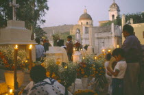 People keeping vigil beside graves decorated with candles and flowers during Night of the DeadDay of the Dead