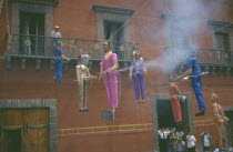 Exploding papier mache figures of Judas hanging from balconies in Plaza Principal during Easter celebrations.