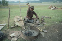 Blacksmith using bellows to fan fire whilst hammering metal