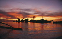 Rocky outcrops and moored boats silhouetted against pink and orange sunset sky reflected in the water