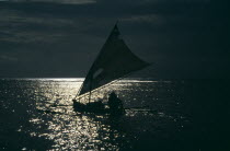 Sailboat silhouetted in early evening sunlight reflected on the water