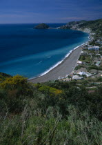 Moronti.  View over sandy beach and nearby buildings from tree and gorse covered hillside.