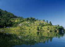 View over Lake Phewa with reflected terraced hillside with houses and trees.
