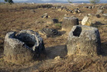 Stone jars of unknown origin in the ground with lids fallen beside them