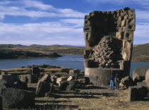 Sillustani.  Pre columbian funeral tower  or chullpa  with two people standing at its base  looking upwards.