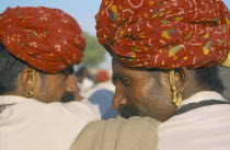 Two men wearing turbans and earrings with backs to camera