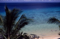 View looking down on sandy beach on the west coast of the island with people bathing and palm trees in the foreground