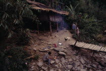 Karen refugee camp house with chickens outside by wooden bridge and boy tending a fire in the foreground