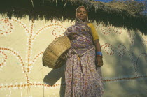 Mithila woman standing in front of painted house.