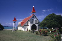 Red and white chapel with garden in the foreground and the sea behind