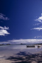 Sandy Beach with moored Boats and an Island in the distance with blue sky and whispy clouds above