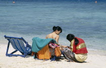 Also known as Coral Island. Japanese tourist sitting in a deck chair on the beach having a manicure