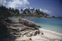 View from beach over rocks toward bay surrounded by rocks and palms