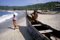 Fisherman tending to his boat moored on the sandy beach with passing man in sarong