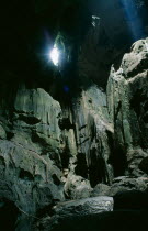 View of rocky interior lit by sunlight pouring through small opening in the roof of the cave