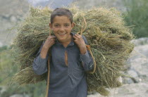 Smiling boy carrying bale of cut grass on his shoulders