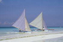 Two outriggers with striped sails moored on the edge of a sandy beach