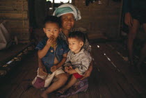Karen Refugee mother sitting with her two children on the floor of a hut