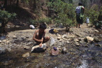 Karen refugee boy washing by a rocky stream