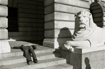 A drunk sleeps on the steps next to a lion statue outside the City Hall in Market Square Black and white image.
