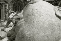A child plays on the statue of a reclining Buddha.  Black and white image.