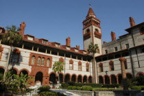 Flagler College  red and white brick building with tower with palm trees and a water feature.