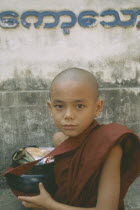 Young novice monk with bowl full of Alms offerings. Myanmar