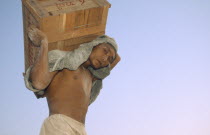 Man carrying a crate above his head  wearing head scarf. Banks of the Irrawaddy Myanmar